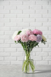 Vase with beautiful aster flower bouquet on table against brick wall