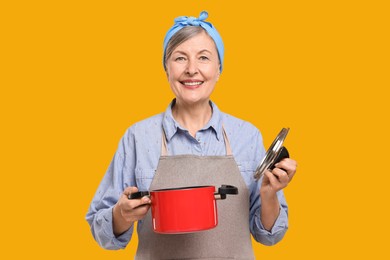 Happy housewife with pot and lid on orange background
