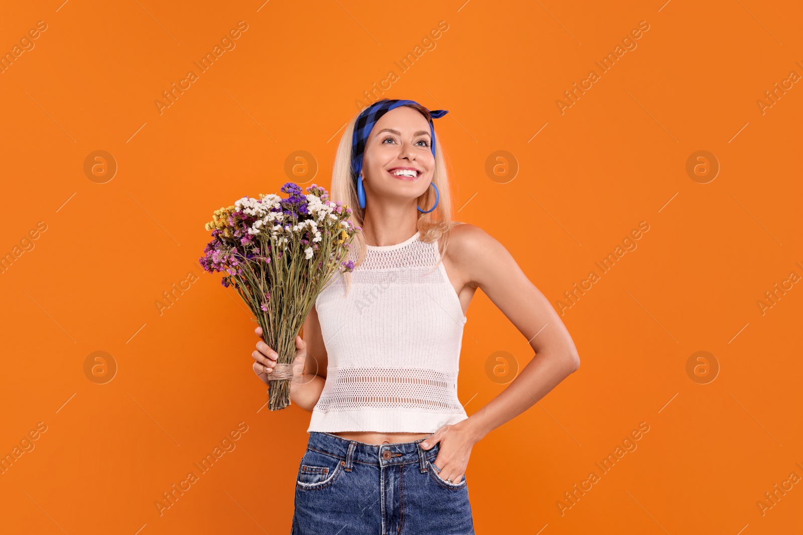 Photo of Happy hippie woman with bouquet of flowers on orange background. Space for text