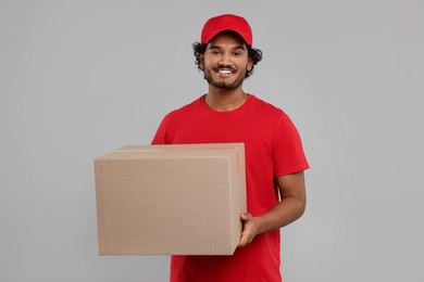Happy young courier with parcel on grey background