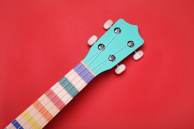 Photo of Colorful ukulele neck on red background, top view. String musical instrument