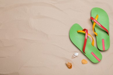 Photo of Pair of green flip flops and sea shells on sand, flat lay. Space for text