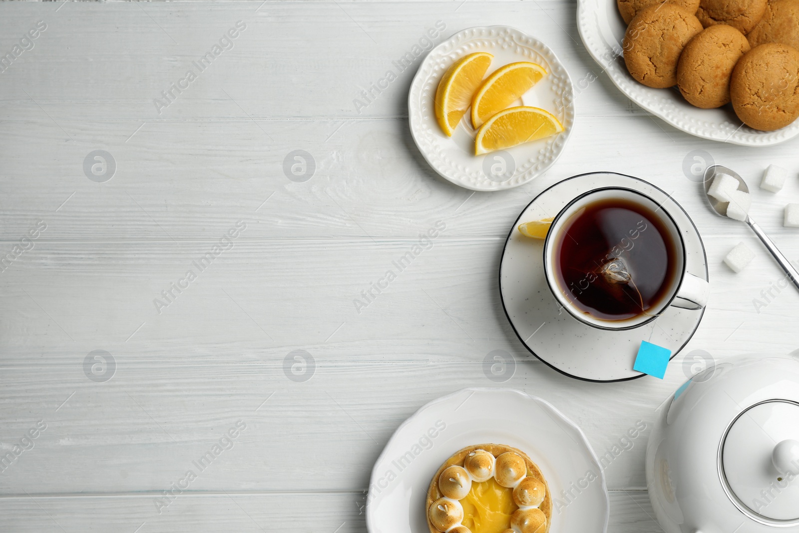 Photo of Flat lay composition with tea bag in cup of hot water on white wooden table, space for text