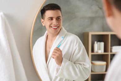 Photo of Happy man with toothbrush near mirror in bathroom