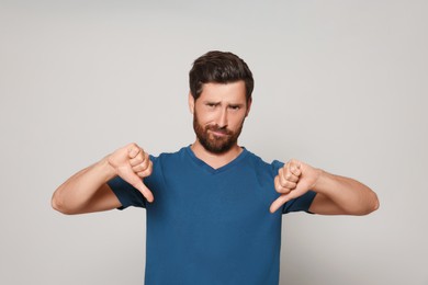 Handsome bearded man showing thumbs down on light grey background