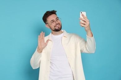 Photo of Handsome man in white jacket and eyeglasses taking selfie on light blue background