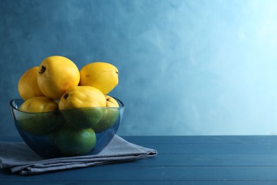 Tasty ripe quinces in bowl on blue wooden table, space for text