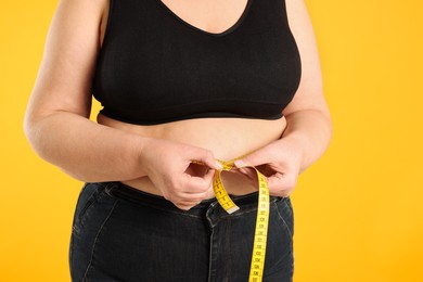 Overweight woman measuring waist with tape on orange background, closeup