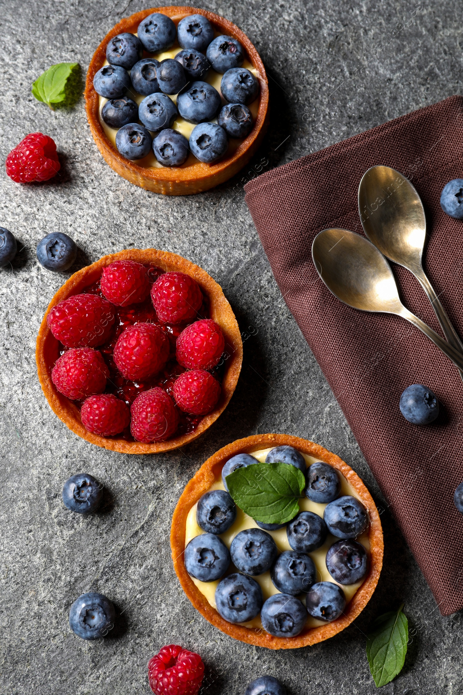 Photo of Tartlets with different fresh berries on light grey table, flat lay. Delicious dessert