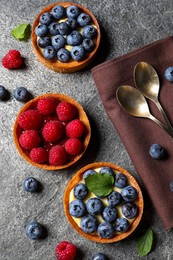 Tartlets with different fresh berries on light grey table, flat lay. Delicious dessert