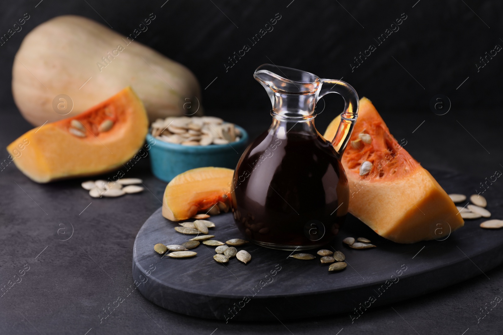 Photo of Fresh pumpkin seed oil in glass jug on dark grey table. Space for text