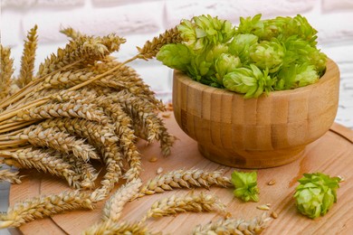 Photo of Fresh green hops and ears of wheat on wooden board, closeup