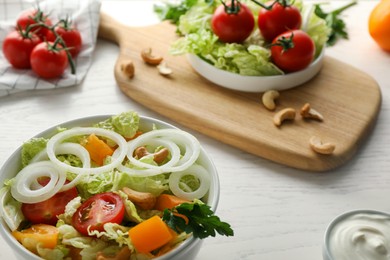 Bowl of delicious salad with Chinese cabbage, tomatoes and onion on white wooden table, closeup