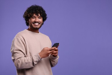 Handsome smiling man using smartphone on violet background, space for text