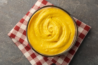 Photo of Tasty mustard sauce in bowl on grey textured table, top view