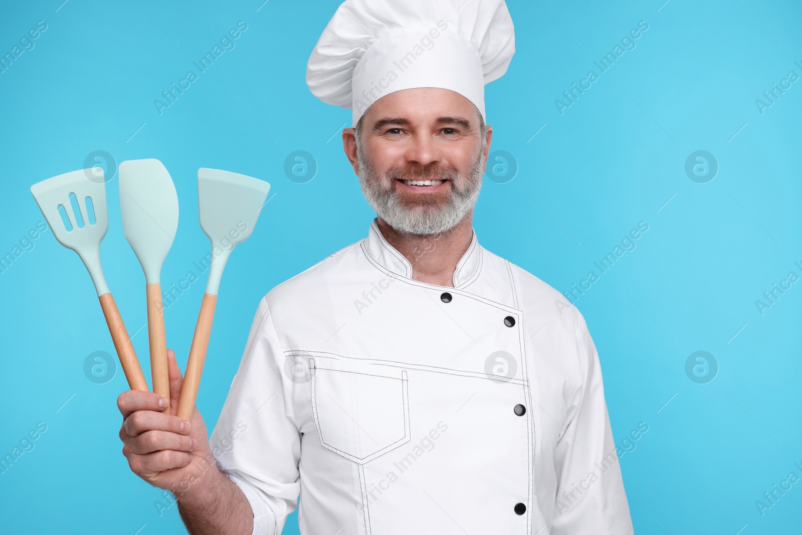 Photo of Happy chef in uniform with kitchen utensils on light blue background