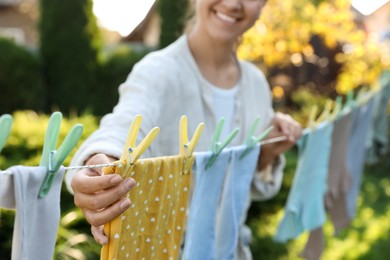 Photo of Closeup view of smiling woman hanging baby clothes with clothespins on washing line for drying in backyard