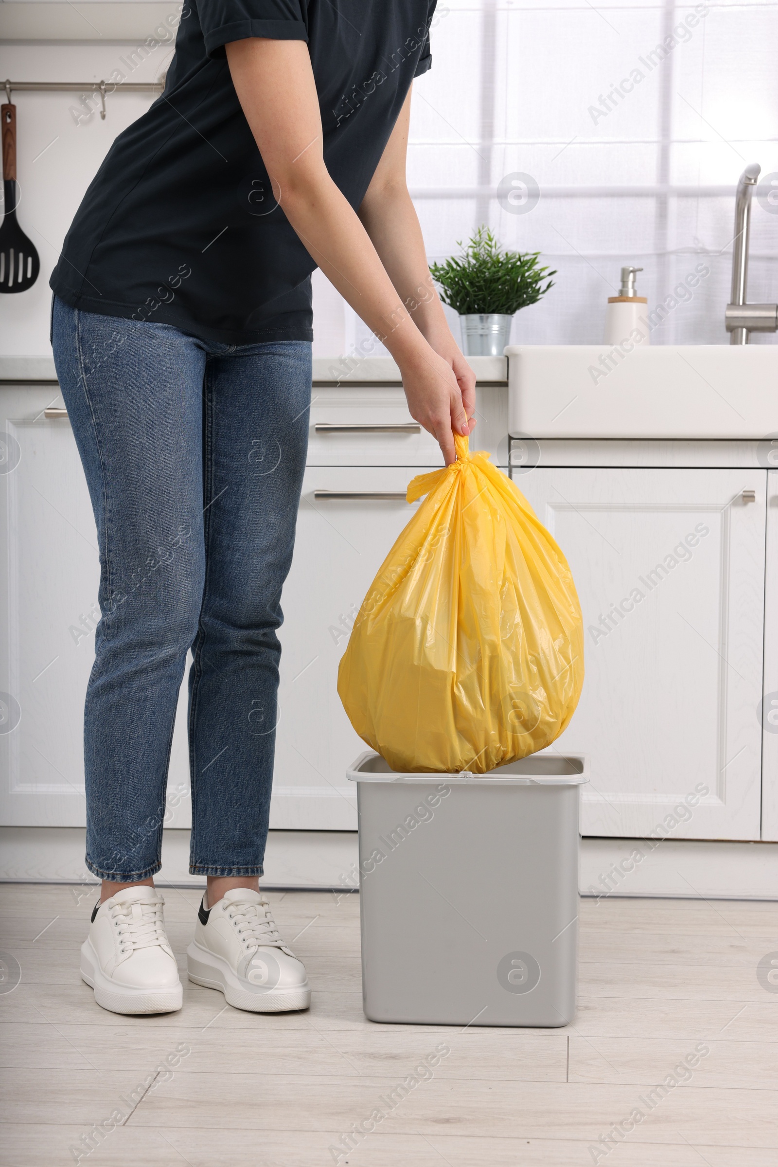 Photo of Woman taking garbage bag out of trash bin in kitchen, closeup