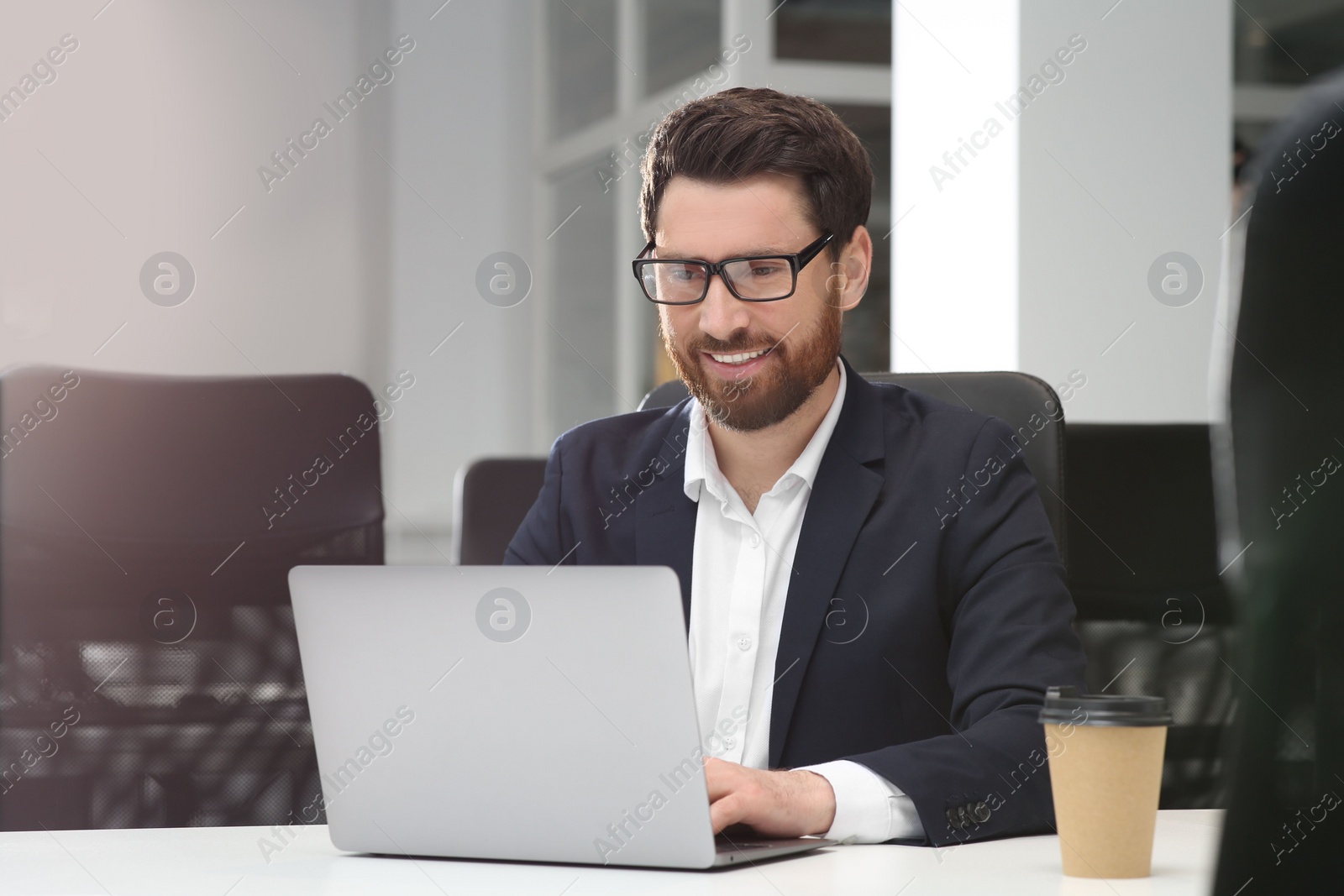 Photo of Man working on laptop at white desk in office