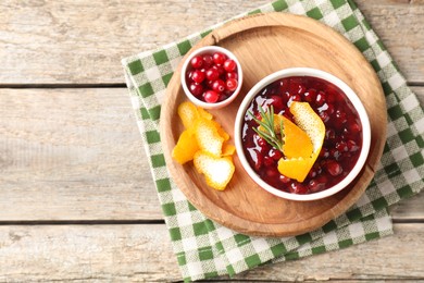 Photo of Cranberry sauce in bowl, fresh berries, rosemary and orange peels on wooden table, top view. Space for text