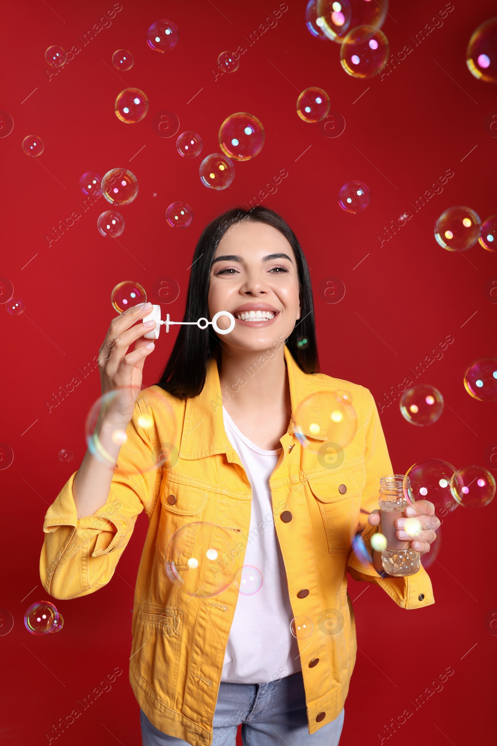 Photo of Young woman blowing soap bubbles on red background