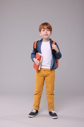 Photo of Happy schoolboy with backpack and books on grey background