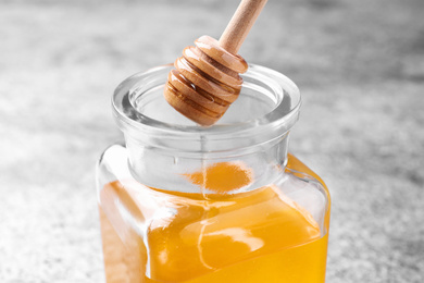 Photo of Dripping tasty honey from dipper into glass on table, closeup