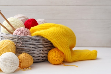 Woolen yarns and knitting needles in basket on white wooden table