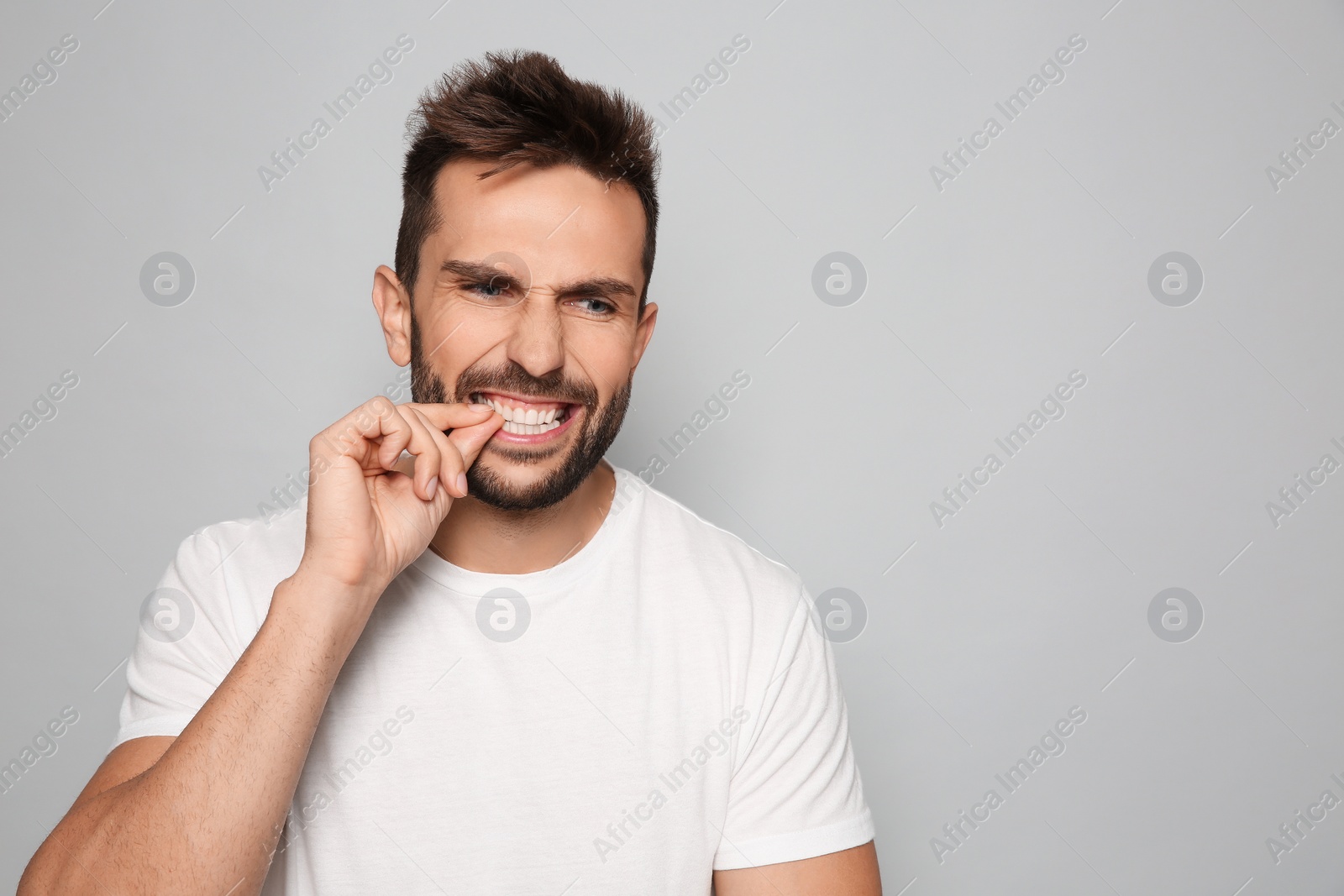 Photo of Man biting his nails on grey background. Space for text