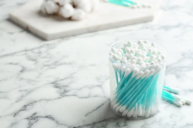 Photo of Plastic container with cotton swabs on marble table. Space for text