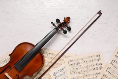 Violin, bow and music sheets on white wooden table, top view
