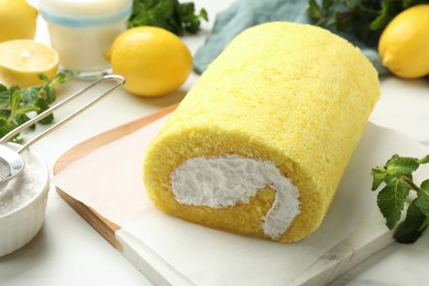 Photo of Delicious cake roll, mint, lemons and powdered sugar on white table, closeup