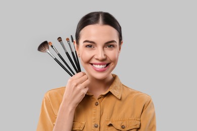 Photo of Happy woman with different makeup brushes on light grey background