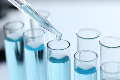 Photo of Dripping liquid from pipette into test tube on blurred background, closeup