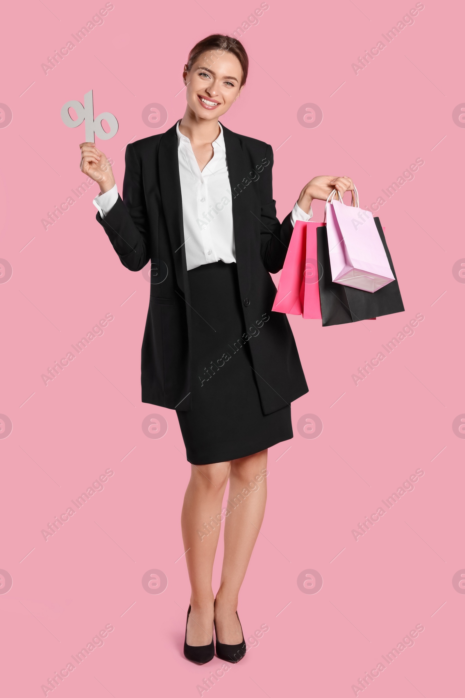 Photo of Happy young woman with shopping bags and percent symbol figure on light pink background. Big sale