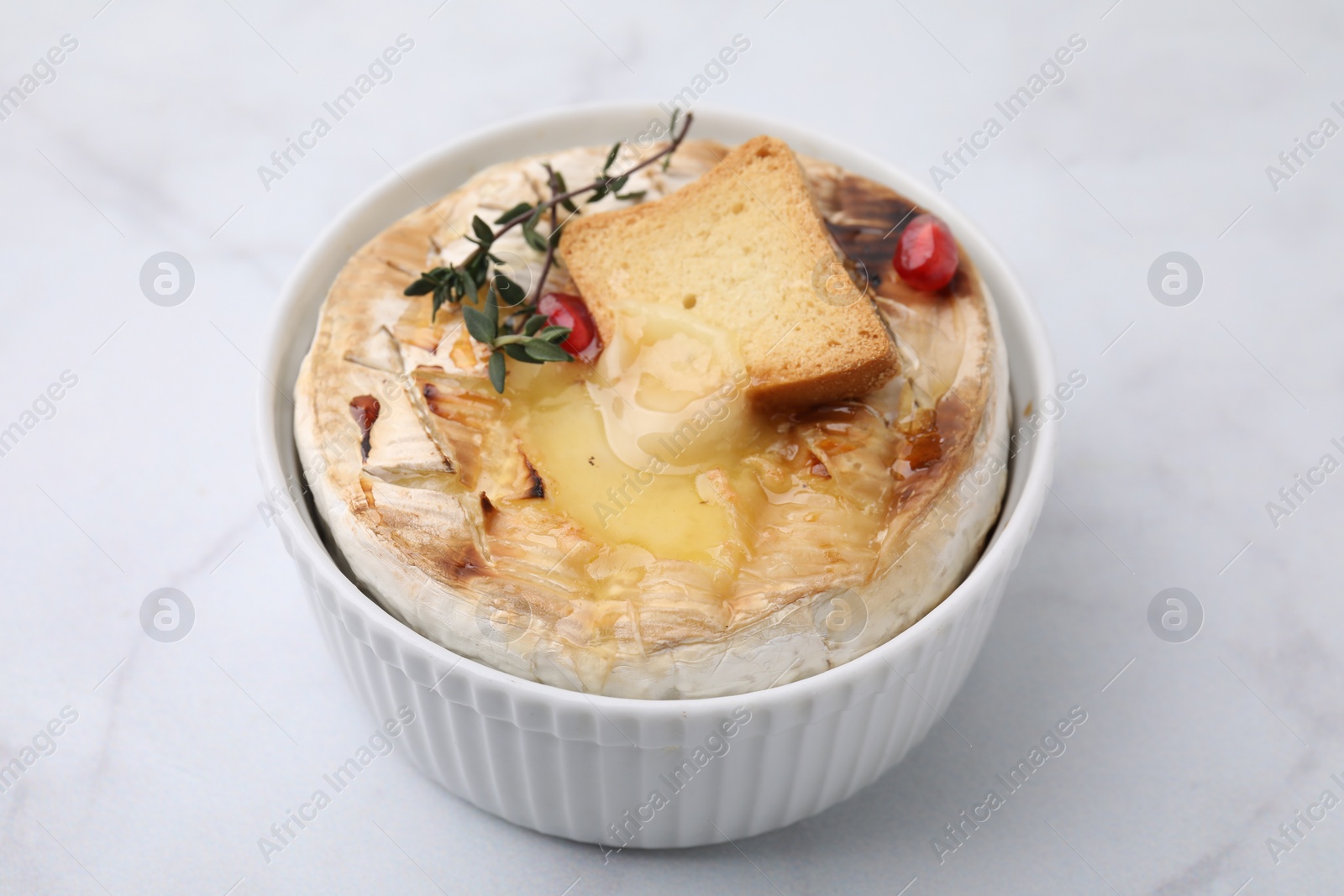 Photo of Tasty baked camembert with crouton and thyme on white marble table, closeup