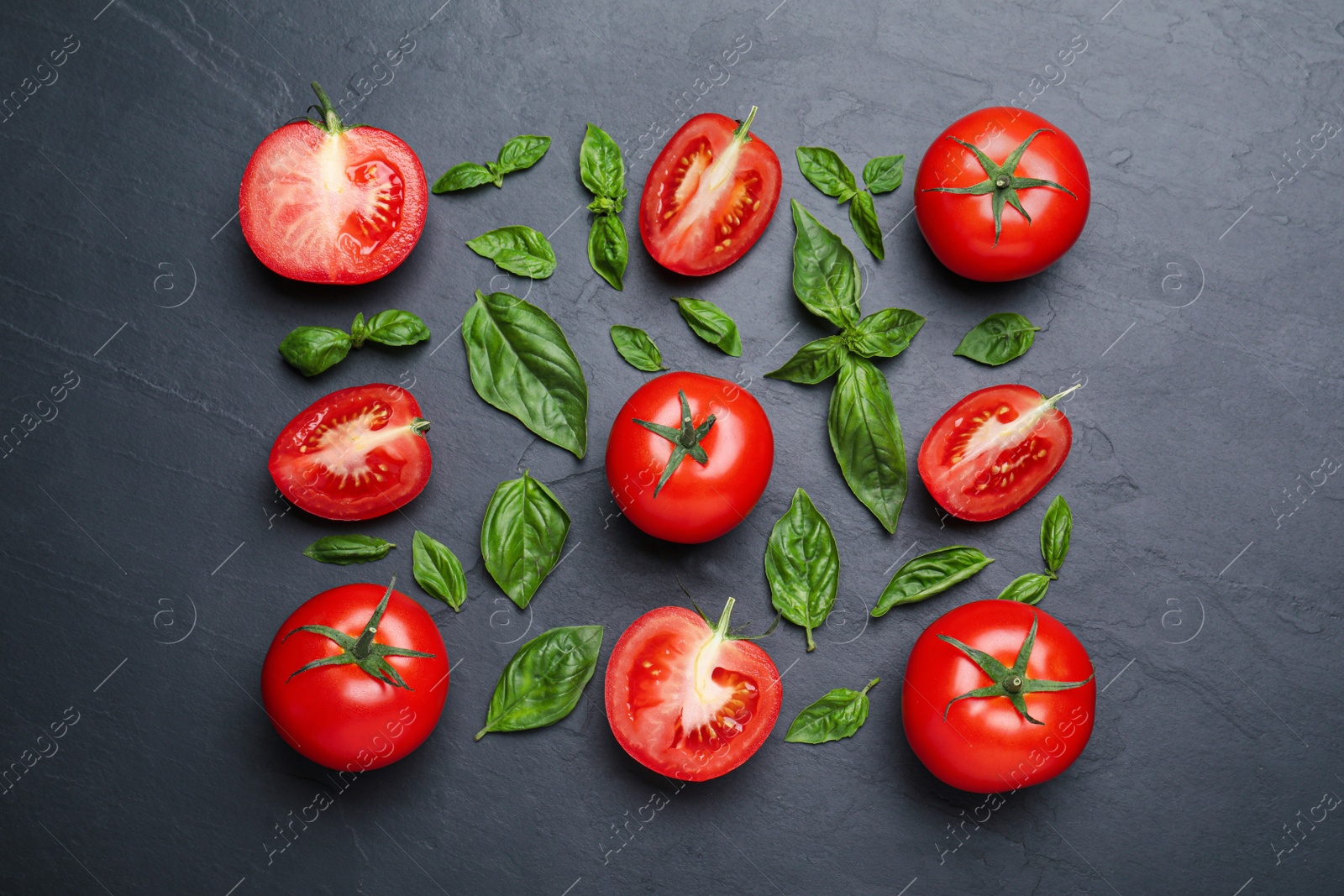 Photo of Fresh basil leaves and tomatoes on black slate table, flat lay