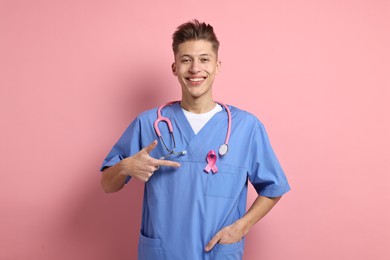 Photo of Mammologist pointing at pink ribbon on color background. Breast cancer awareness