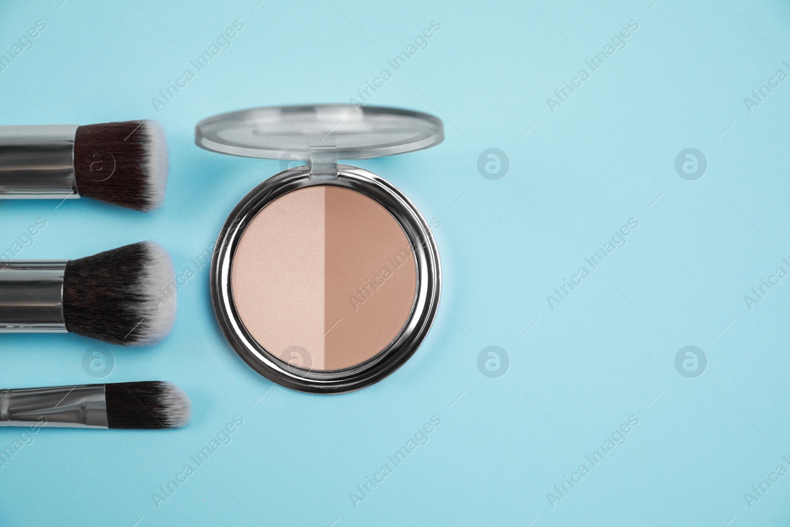 Photo of Face powder and brushes on light blue background, flat lay. Space for text