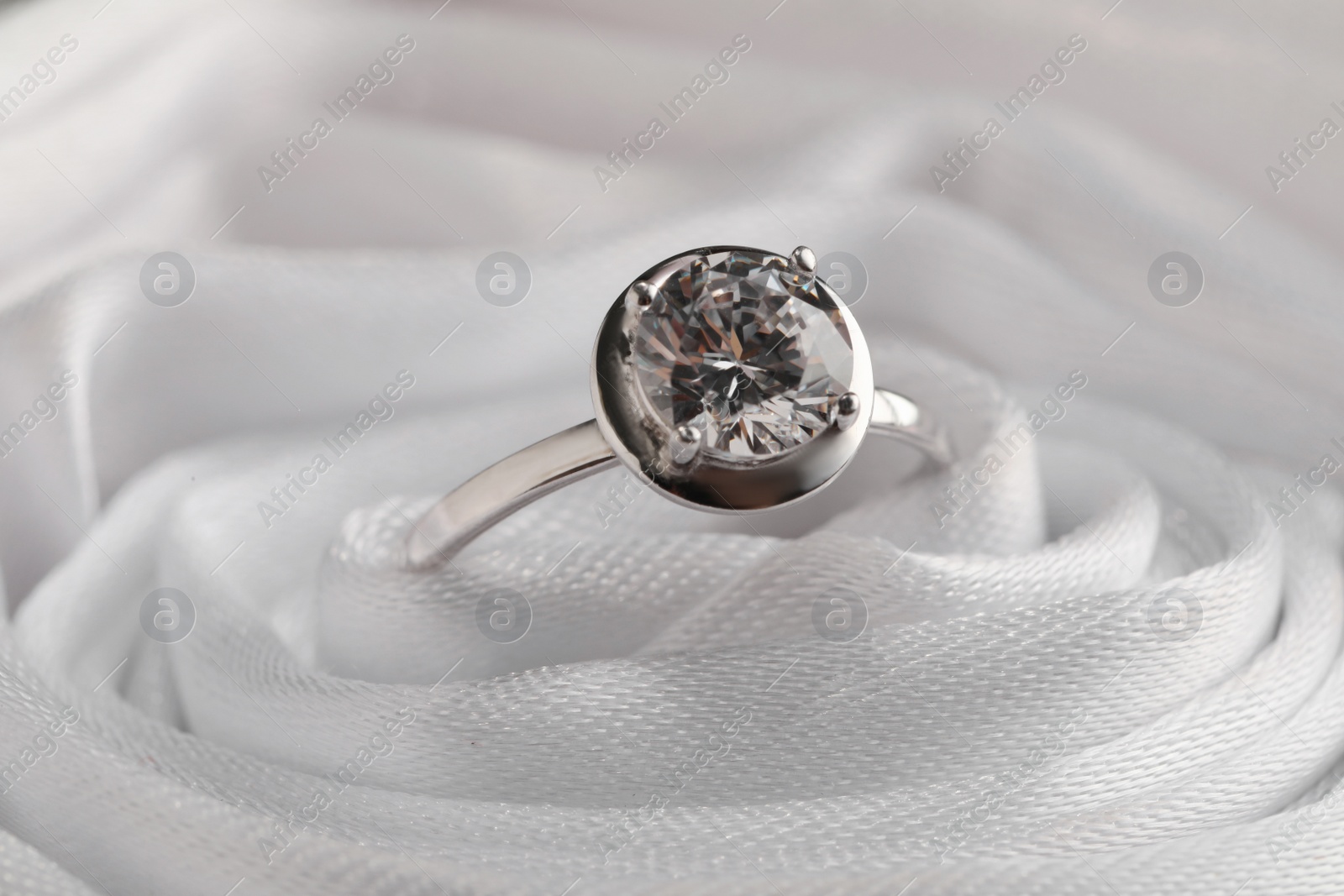 Photo of Beautiful engagement ring in white fabric, closeup view