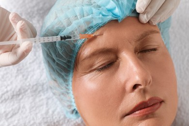 Doctor giving facial injection to senior woman in clinic, closeup. Cosmetic surgery