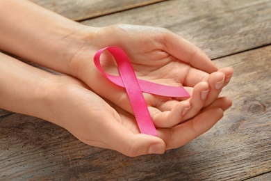 Photo of Woman holding pink ribbon on wooden background, closeup. Cancer awareness