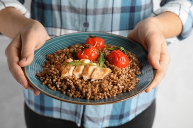 Woman holding plate of buckwheat porridge with meat and tomatoes, closeup