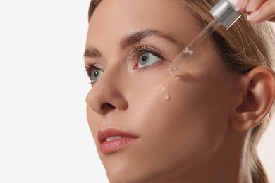 Beautiful woman applying cosmetic serum onto her face on white background, closeup