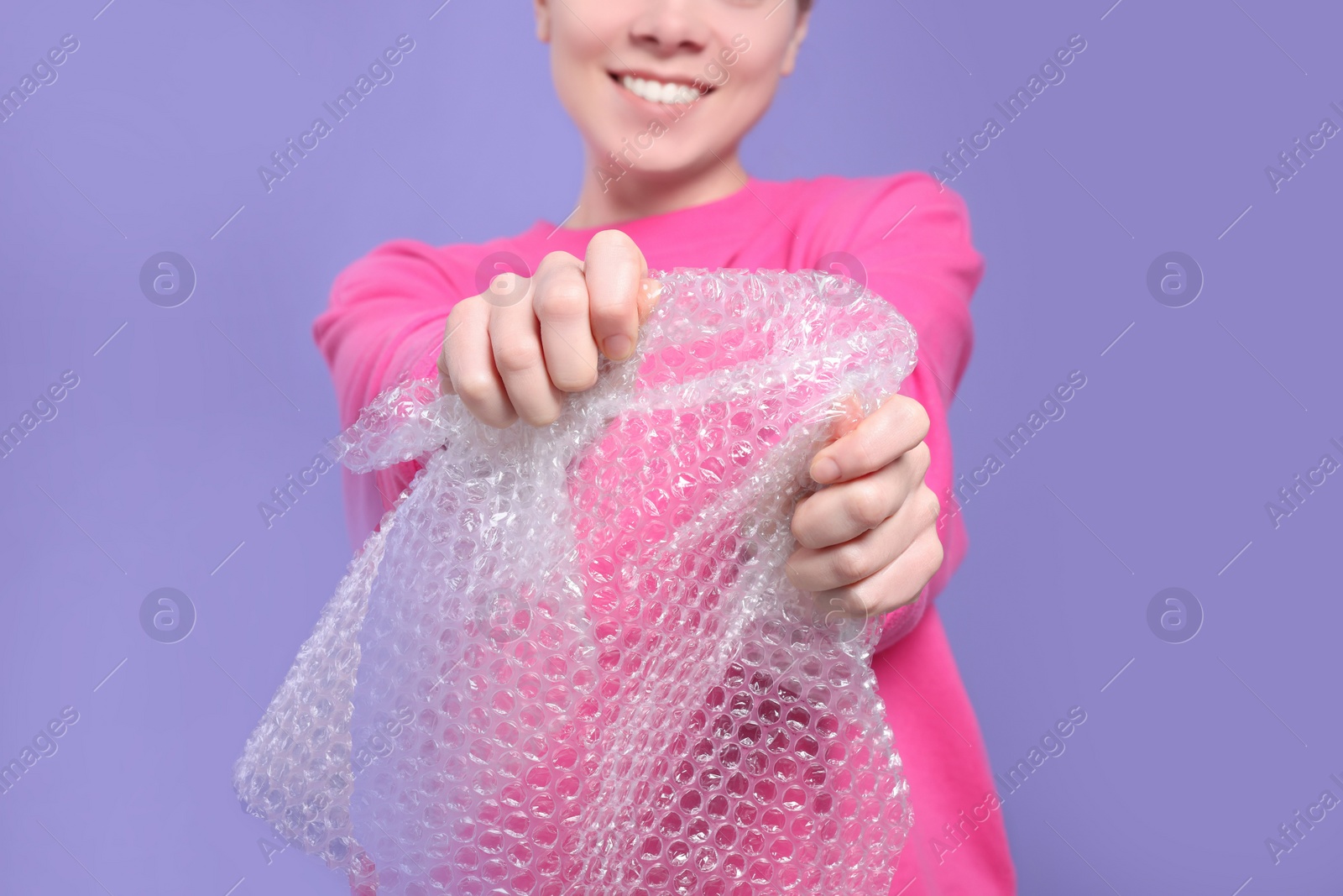 Photo of Woman popping bubble wrap on purple background, closeup. Stress relief