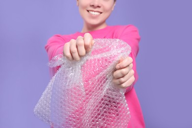 Photo of Woman popping bubble wrap on purple background, closeup. Stress relief