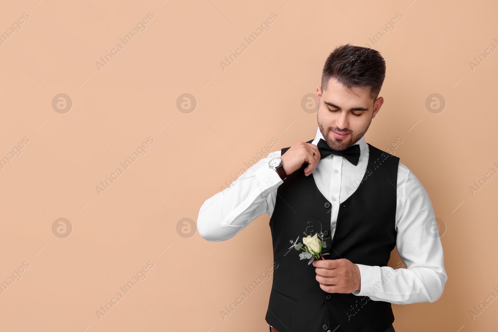 Photo of Handsome young groom with boutonniere on beige background, space for text. Wedding accessory