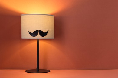 Man's face made of artificial mustache and lamp on terracotta background. Space for text