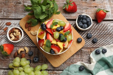 Photo of Tasty fruit salad in bowl and ingredients on wooden table, flat lay