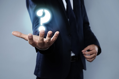 Image of Businessman demonstrating question mark symbol on grey background, closeup